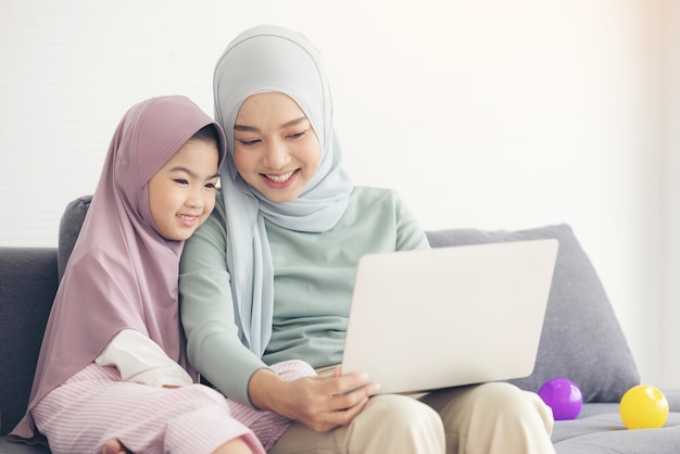 Asian muslim mother and daughter smiling when using laptop together