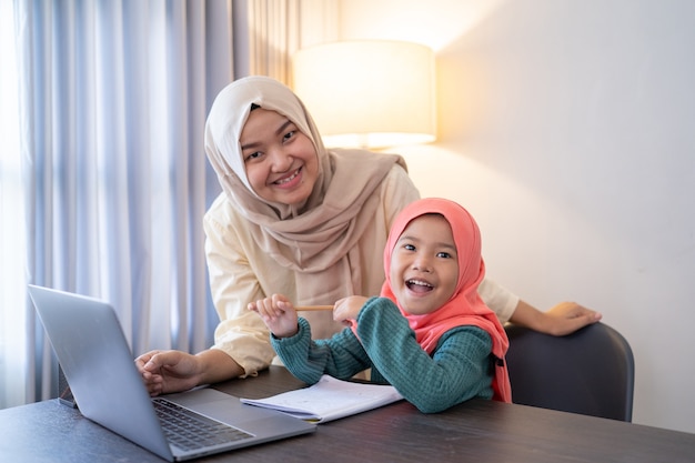 Asian muslim mother help her daughter to learn online using laptop studying from home