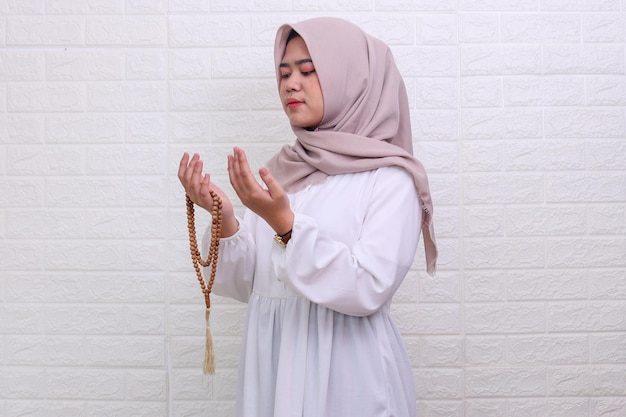 Asian muslim teenager in a veil holding prayer beads and gesturing pray