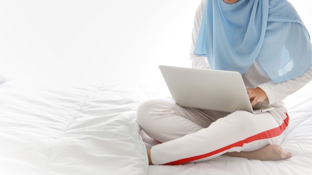 Asian muslim woman hands use laptop sitting on bed in bedroom. 