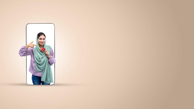 Asian Muslim woman in a headscarf holding a credit card on a mobile phone screen