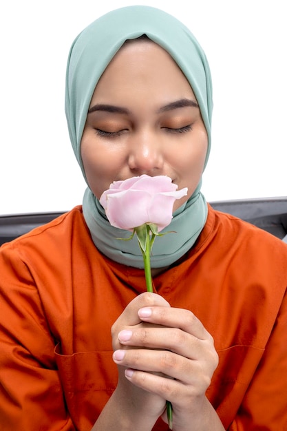 Asian Muslim woman in a headscarf sitting in a suitcase while holding a pink rose flower