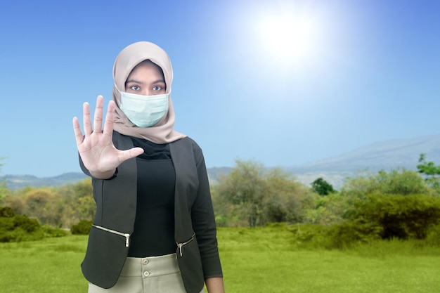 Asian Muslim woman in a headscarf and wearing a face mask showing a stop sign