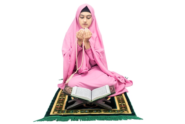 Asian Muslim woman in a veil sitting while raised hands and praying with prayer beads isolated over white background