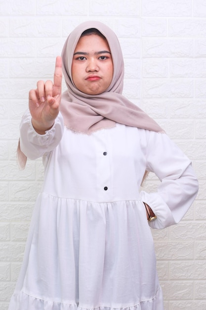 Asian Muslim woman wearing hijab showing stop gesture at the camera with an angry expression