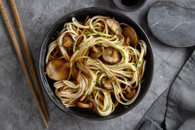 Asian noodles soup with mushrooms shiitake served in dark bowl. Closeup