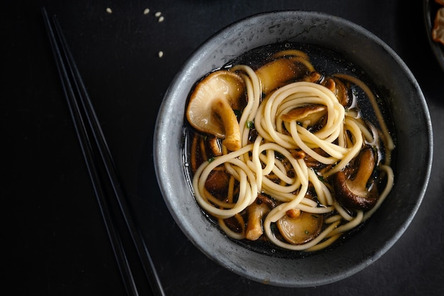 Asian noodles soup with mushrooms shiitake served in dark bowl. Closeup