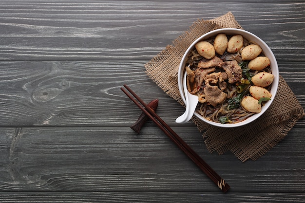 Asian noodles with pork, pork balls, chopsticks and vegetables on dark