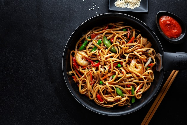 Asian noodles with prawns and vegetables served on pan on dark background.