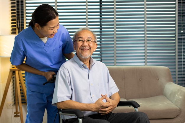 Asian Nurse take care Elderly Senior Man with warm welcome 70s Mature Man patient has good health and support help by Caregiver from medical hospital Grandfather sit on wheelchair copy space