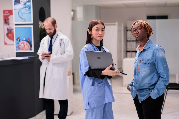 Asian nurse, young african american woman portrait at hospital waiting room. Doctor showing patient medication to female relative. Healthcare professional checking program on smartphone in sanatorium.