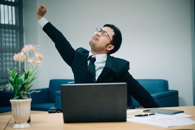 Asian officer man stretching body at the desk of office from back angleThailand peopleBusinessman tired from hard work