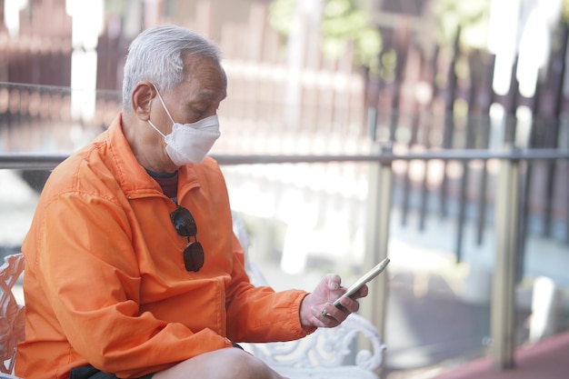 Asian old elder senior man elderly wearing mask using mobile smart phone cellphone outdoor mature retirement lifestyle