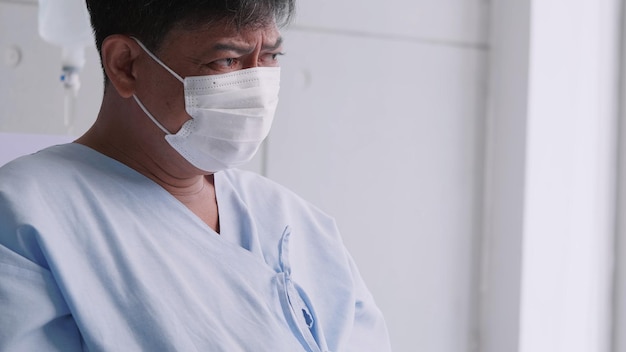 Asian old man is hospitalized with COVID19 Old male patient wearing a medical mask sits on the patient's bed