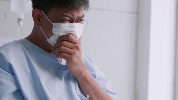 Asian old man is hospitalized with COVID19 Old male patient wearing a medical mask sits on the patient's bed