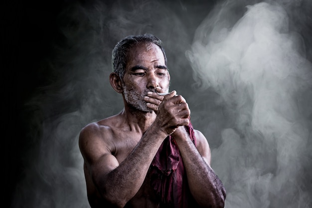 Asian old man smoking cigarette and the smoke released from the mouth against dark