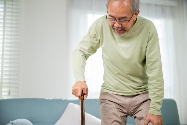 Asian Old man with eyeglasses typing to stand up from sofa with walking cane