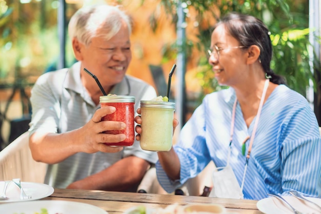 Asian old senior couples raise a glass of fruit juice to drink at cafe background on weekend vacation.Concept of happy living for the elderly.