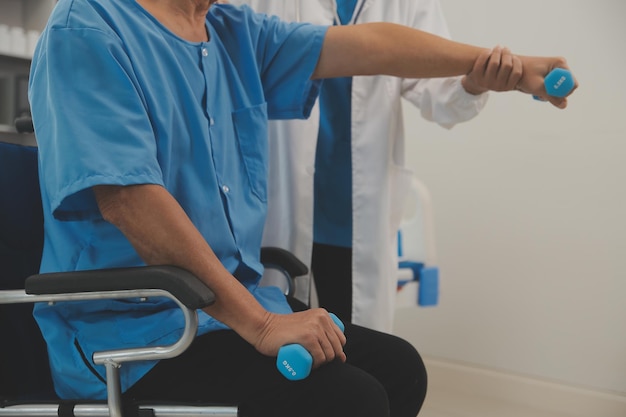 Photo asian older aged man doing physiotherapist with support from nurse senior elderly male sitting on sofa in living room using dumbbells workout exercise for patient with caregiver in nursing care