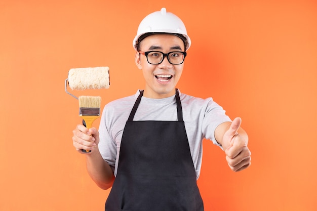 Asian painter holding paint brush posing on orange wall