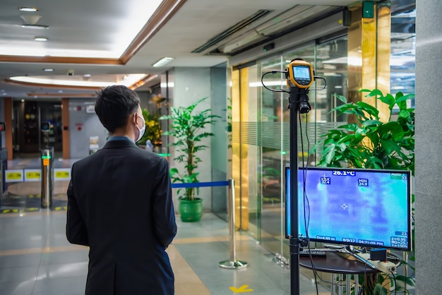 Asian people waiting for body temperature check before access to the building by thermoscan or infrared thermal camera