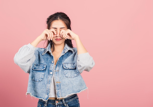 Asian portrait beautiful cute young woman wear denim bad mood her cry wipe tears with fingers, studio shot isolated on pink background, Thai female feeling sad unhappy crying with copy space