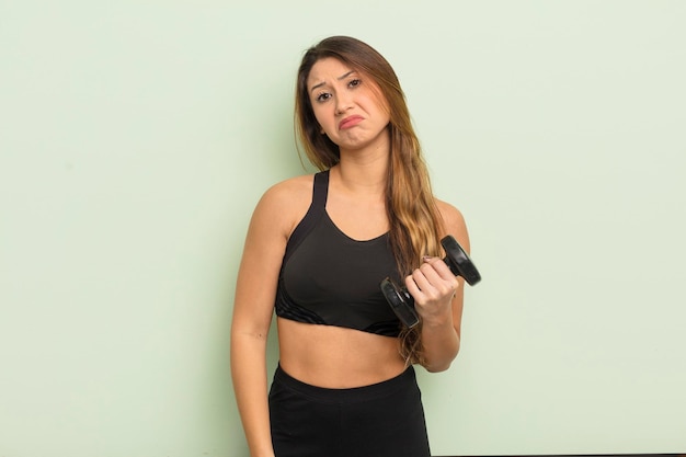 Asian pretty woman feeling sad and whiney with an unhappy look and crying fitness concept with a dumbbell