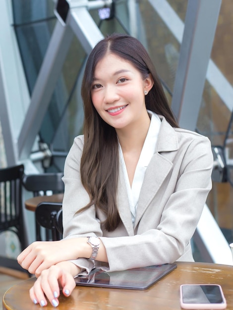 Asian professional business woman in cream colored suit happily on tablet while in coffee shop.