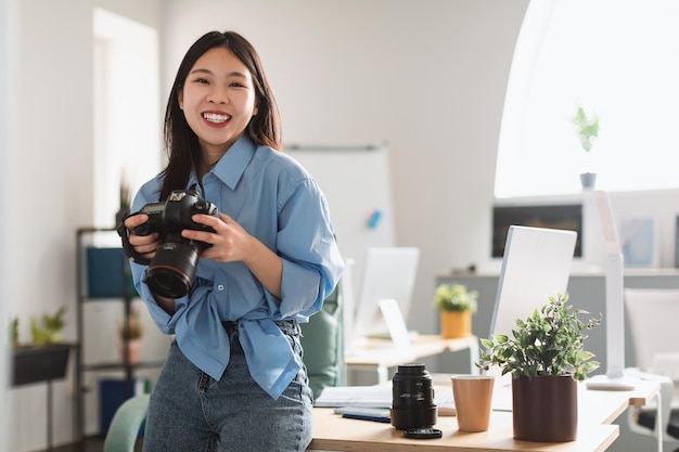 Asian Professional Photographer Woman Holding Camera Standing In Photo Studio