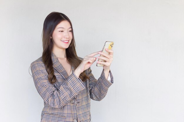 Asian professional woman with black long hair wearing plaid suit and pretty happily using smartphone