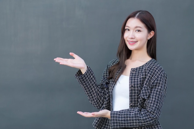 Asian professional working woman who wears black suit with braces on teeth is pointing hand.