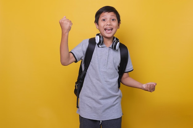 Asian school boy in casual style use black backpack and headphone against yellow background Back t