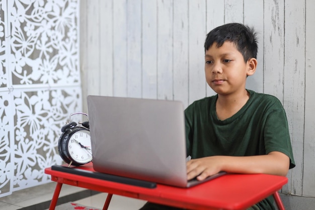 Asian schoolboy studying at home using a laptop and study online with video call teacher at home.