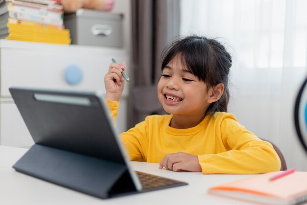 Asian schoolgirl doing her homework with digital tablet at home Children use gadgets to study Education and distance learning for kids Homeschooling during quarantine Stay at home