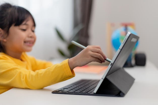 Asian schoolgirl doing her homework with digital tablet at home Children use gadgets to study Education and distance learning for kids Homeschooling during quarantine Stay at home