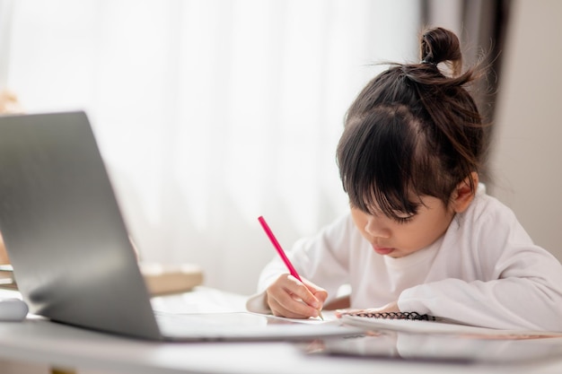 Asian schoolgirl doing her homework with laptop at home Children use gadgets to study Education and distance learning for kids Homeschooling during quarantine Stay at home