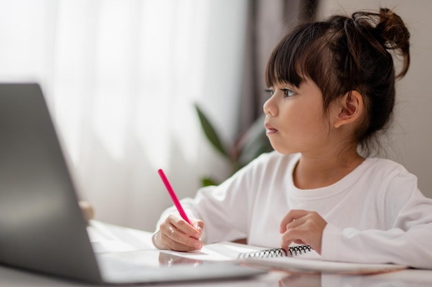 Asian schoolgirl doing her homework with laptop at home Children use gadgets to study Education and distance learning for kids Homeschooling during quarantine Stay at home