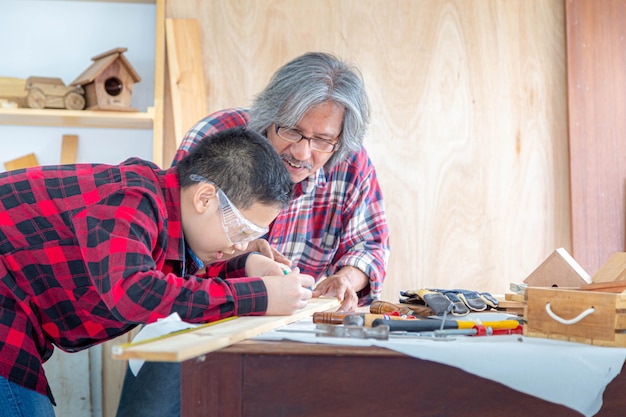 Asian senior carpenter man teaching asian boy craftswoman measuring size of wooden at carpentry shop. Family; carpentry; woodwork and kid concept.