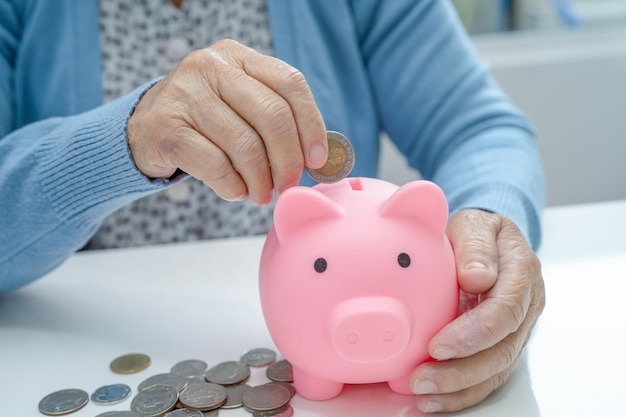 Asian senior or elderly old lady woman holding counting coin money in piggy bank. Poverty, saving problem  in retirement.