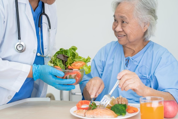 Asian senior or elderly old lady woman patient eating breakfast vegetable healthy food with hope and happy while sitting and hungry on bed in hospital.