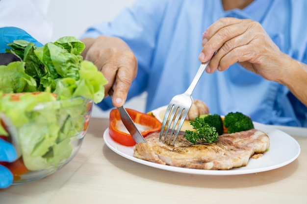 Asian senior or elderly old lady woman patient eating breakfast and vegetable healthy food with hope and happy while sitting and hungry on bed in hospital