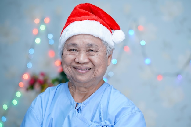 Asian senior or elderly old lady woman patient with Santa Claus helper hat in Christmas and new year celebration festival holiday party in hospital.