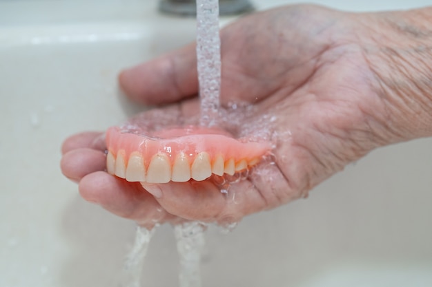 Asian senior or elderly old woman patient holding partial denture of replacement teeth.