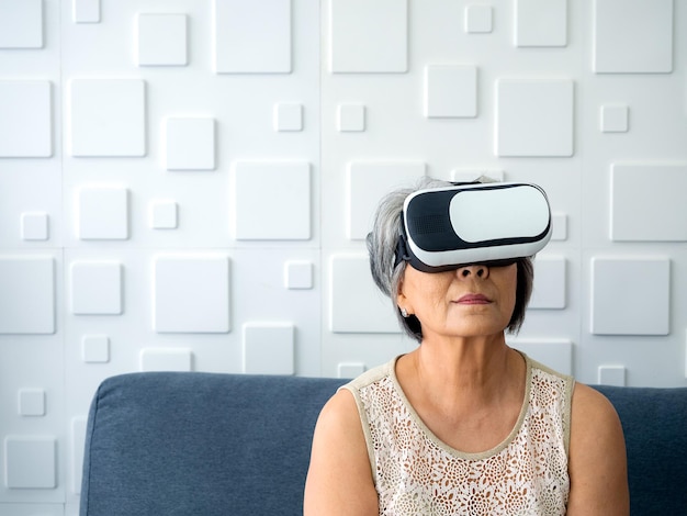 Asian senior female the grandma wearing VR glasses Retired woman white hair holding VR goggles in her hands and exciting while watching via glasses Reality virtual technology lifestyle concept