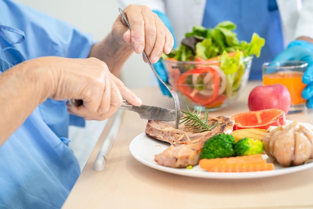 Asian senior old lady woman patient eating breakfast and vegetable healthy food with hope and happy while sitting and hungry on bed in hospital