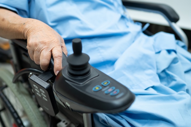 Asian senior woman patient on electric wheelchair with remote control at hospital.