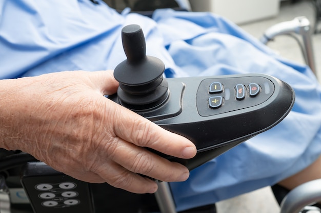 Asian senior woman patient on electric wheelchair with remote control.