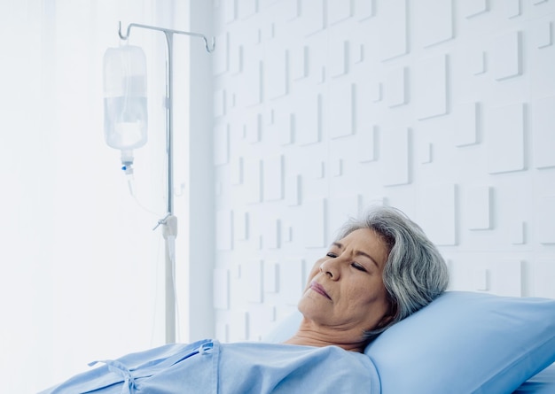 Asian senior woman patient grey hair sleeping on bed in modern white hospital room An old lady is sick and lying on the patient bed recovering on saline drip solution