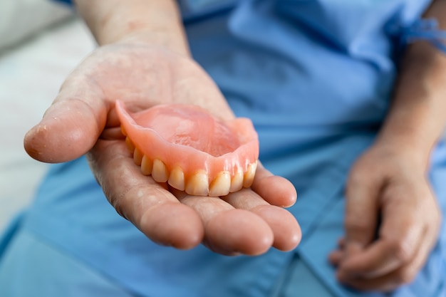 Asian senior woman patient holding denture in hospital.