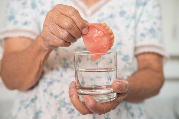 Asian senior woman patient holding and washing denture in water cleanser glass for good chewing